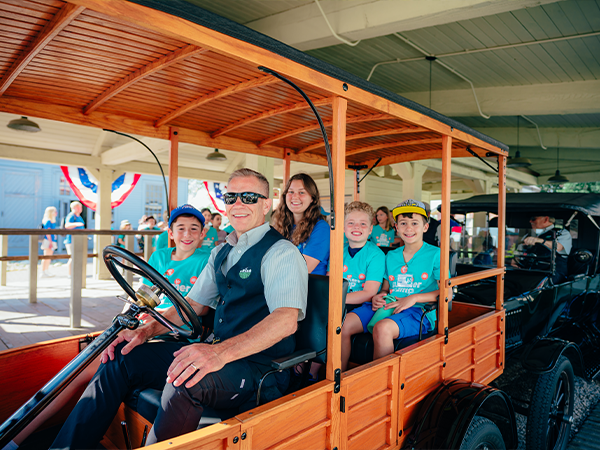Students in blue shirts riding in a wooden Model-T car